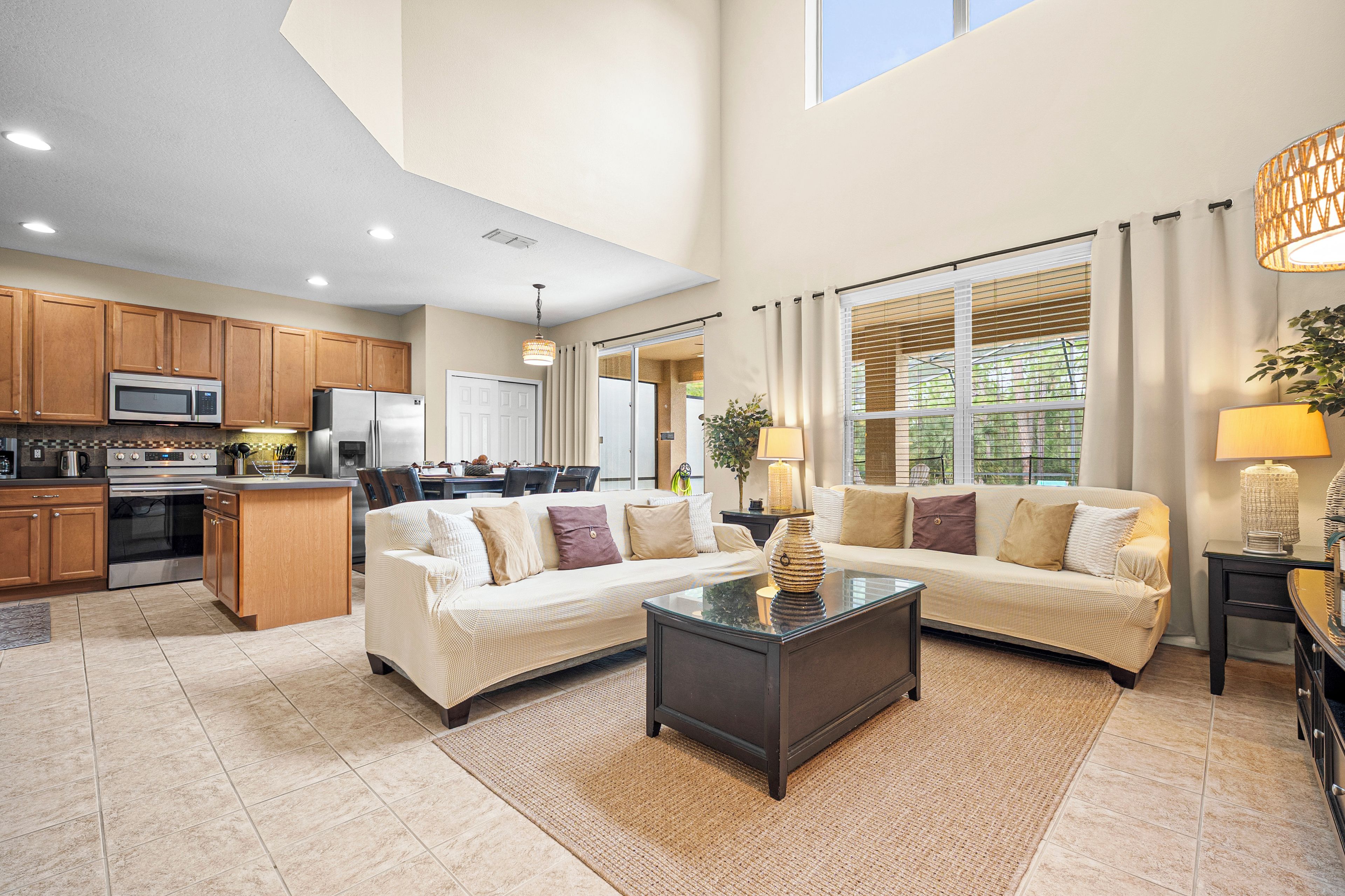 A spacious living room with a large sectional sofa, a coffee table, and a kitchen area with wooden cabinets and appliances.