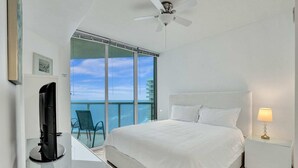 Una habitación de hotel moderna con una cama grande, un escritorio con ordenador, una silla junto a la ventana y un balcón con vistas al horizonte de la ciudad.