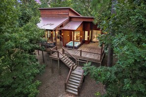 A wooden cabin with a deck, a hot tub, and a staircase leading to the upper level. - Cabin Retreat with Spa, Fire Pit & Games - Sleeps 4 (Broken Bow)