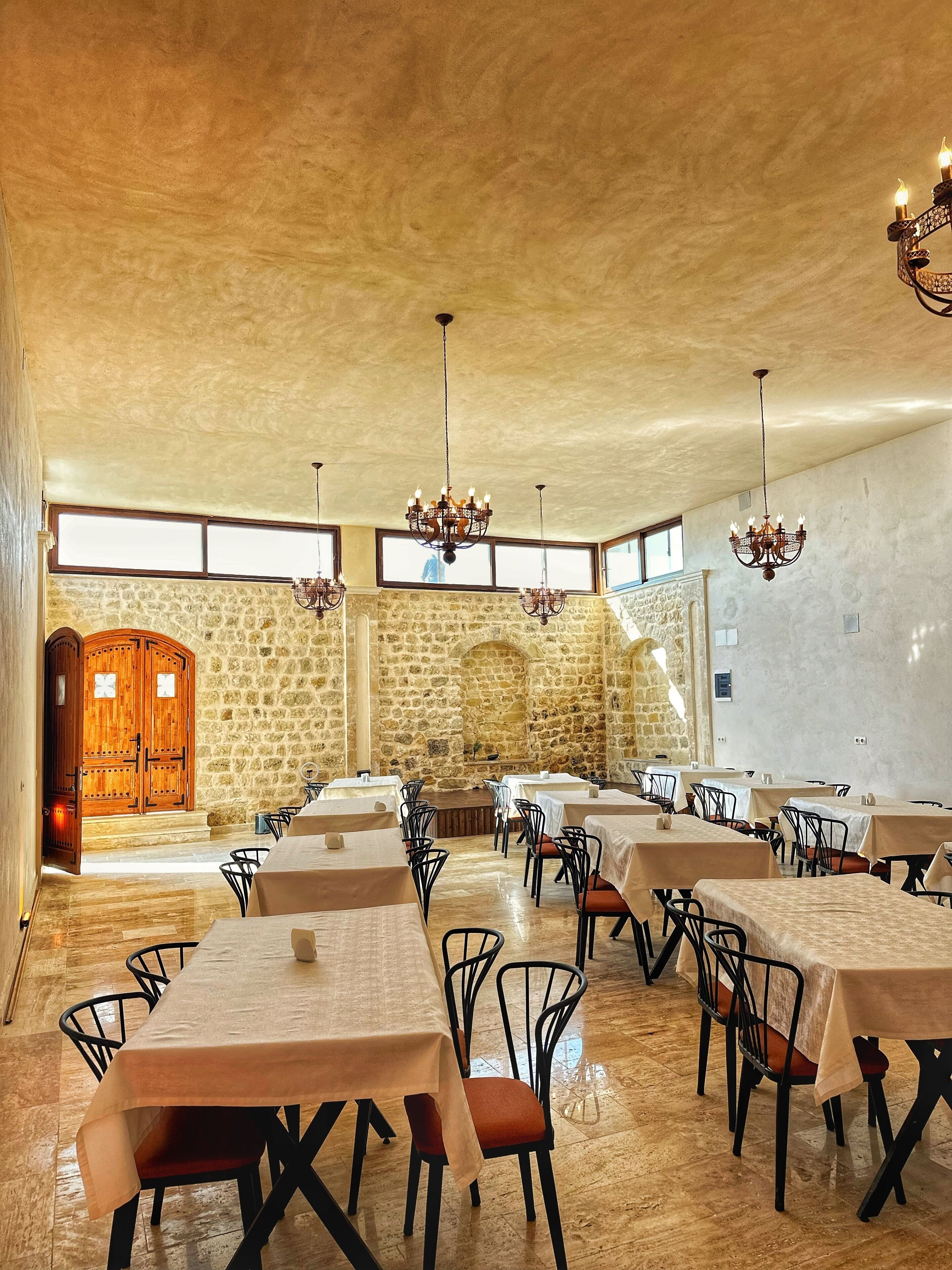 A spacious dining area with multiple tables and chairs, stone walls, and a wooden door.