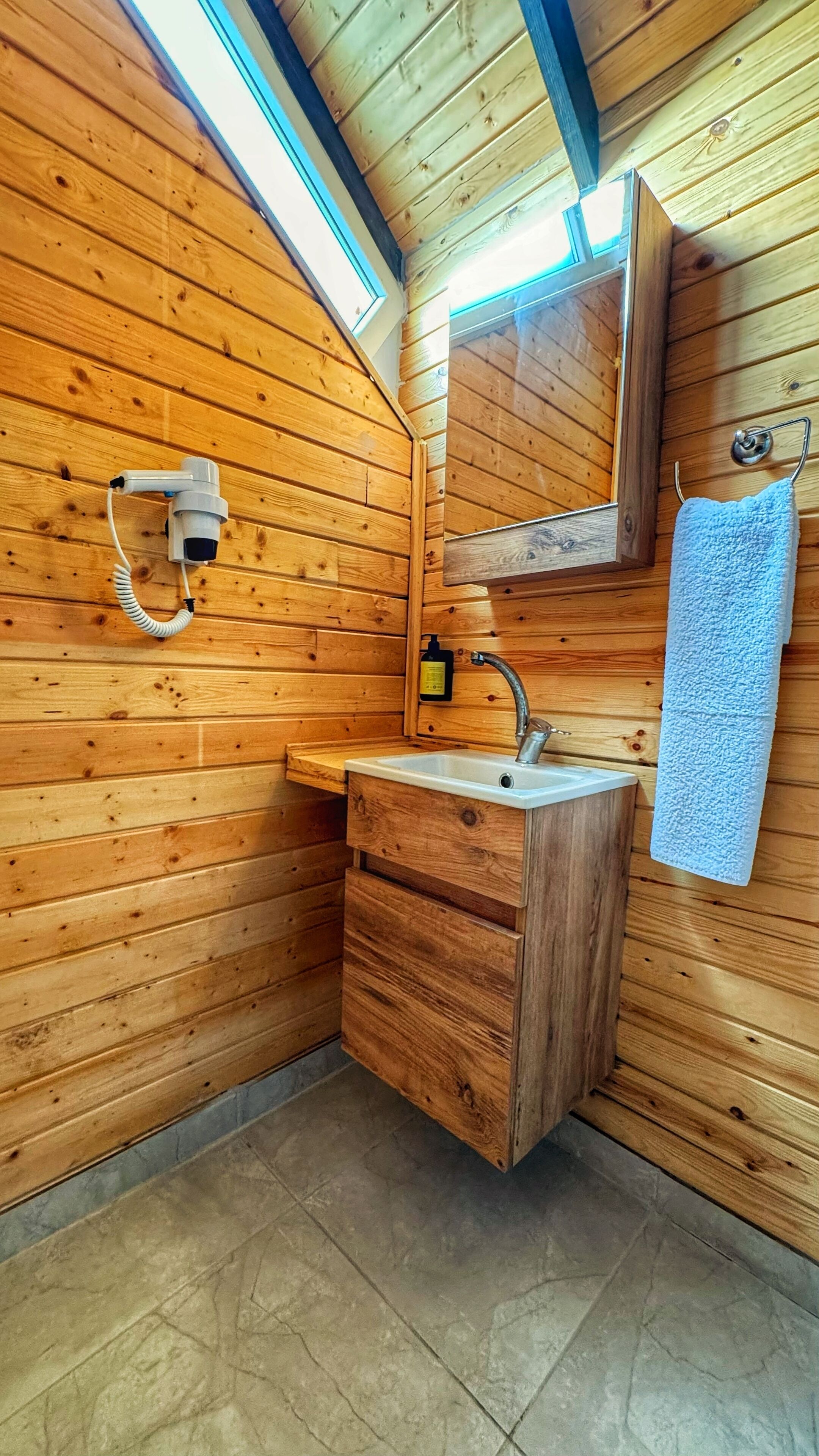 A wooden cabin bathroom with a sink, mirror, towel rack, and a skylight.