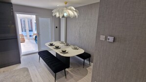 Ein moderner Essbereich mit einem runden Tisch, gedeckt für vier Personen, schwarzen Polsterbänken, einer weißen Feder-Pendelleuchte und Blick auf einen Balkon durch eine Glastür.