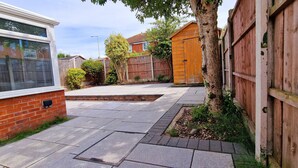 Ein Wohngarten mit gepflasterter Terrasse, Holzlattenzaun und Backsteinmauer.