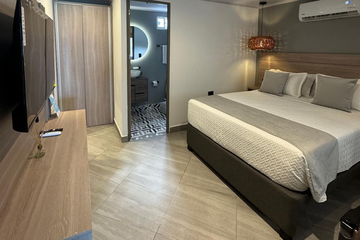 Quarto de hotel moderno com uma cama grande, televisão de tela plana, escrivaninha e ar condicionado.