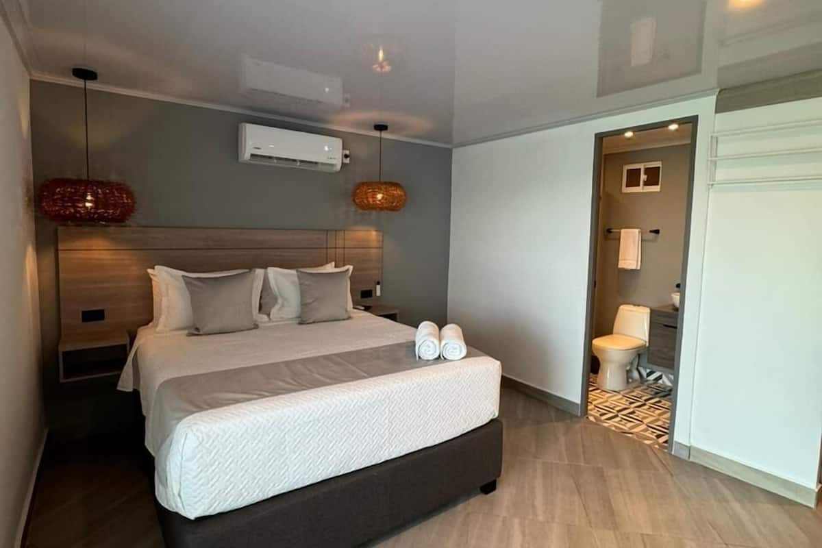 Quarto moderno com cama grande, mesa de cabeceira, luminária pendente e ar condicionado.