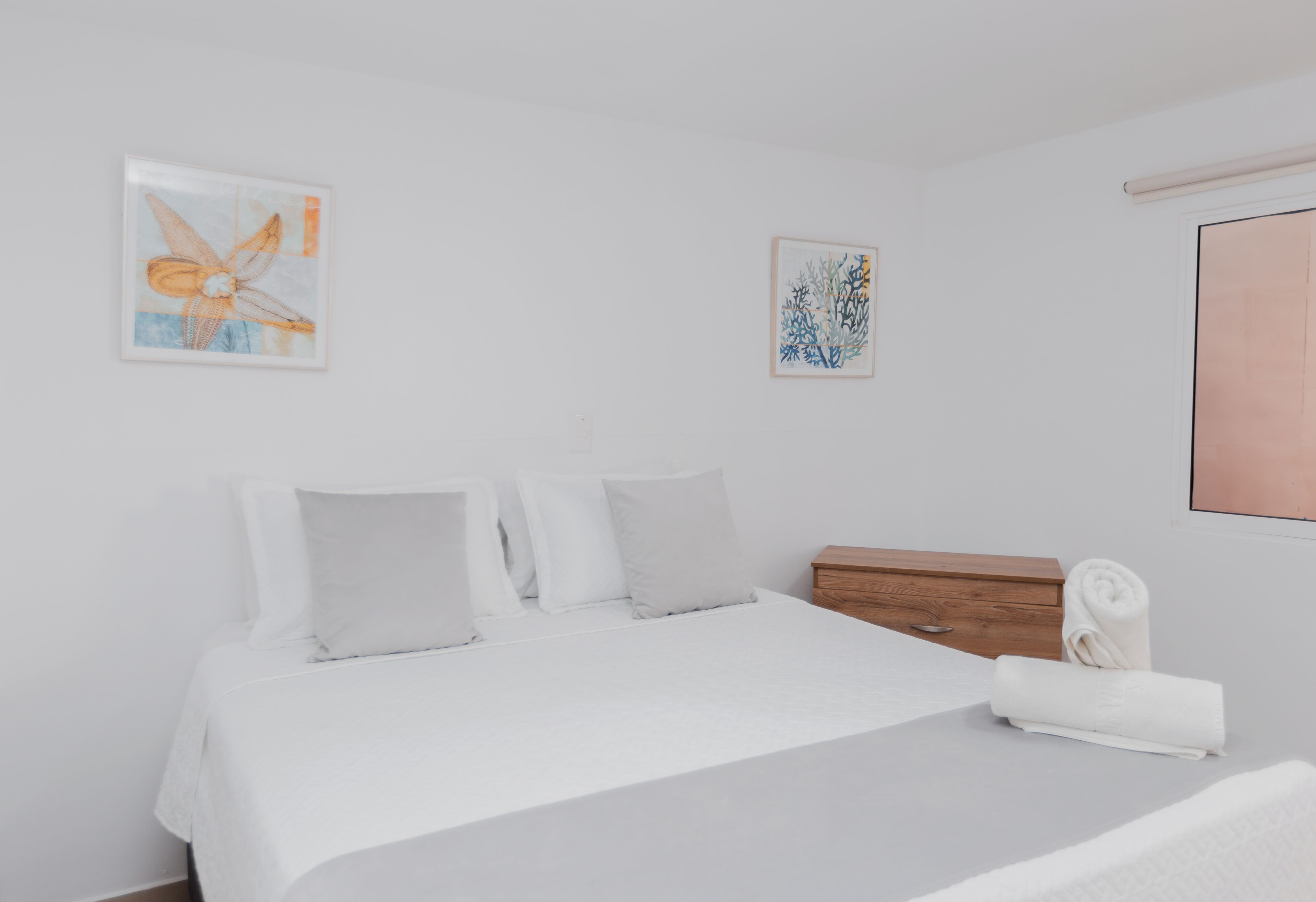 Una camera da letto con un letto, cuscini, un comodino in legno e due opere d'arte appese alle pareti.