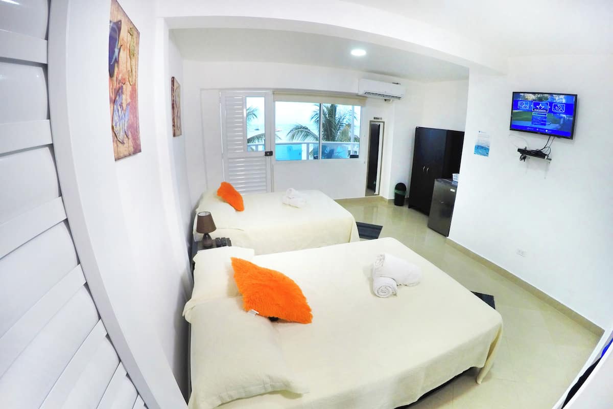 Quarto de hotel com duas camas, uma televisão montada na parede e vista para o exterior pela janela.