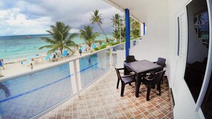 Un balcón con vista a la playa, una piscina y palmeras.