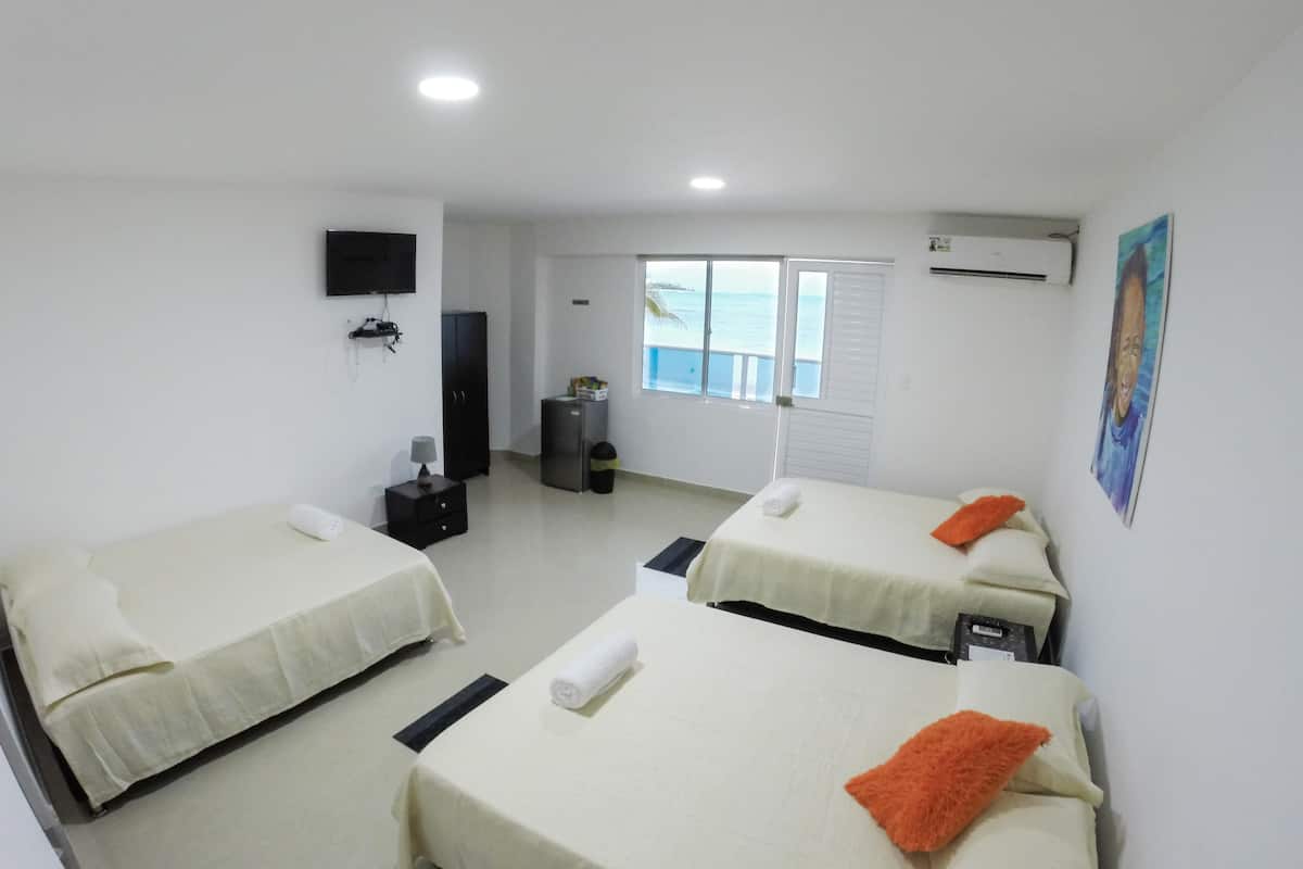 Quarto de hotel com duas camas, televisão, guarda-roupa, uma mesinha e janela com vista para o mar.