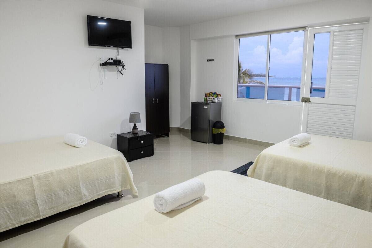 Quarto de hotel com duas camas, televisão, guarda-roupa, mini-frigorífico e janela com vista para o mar.