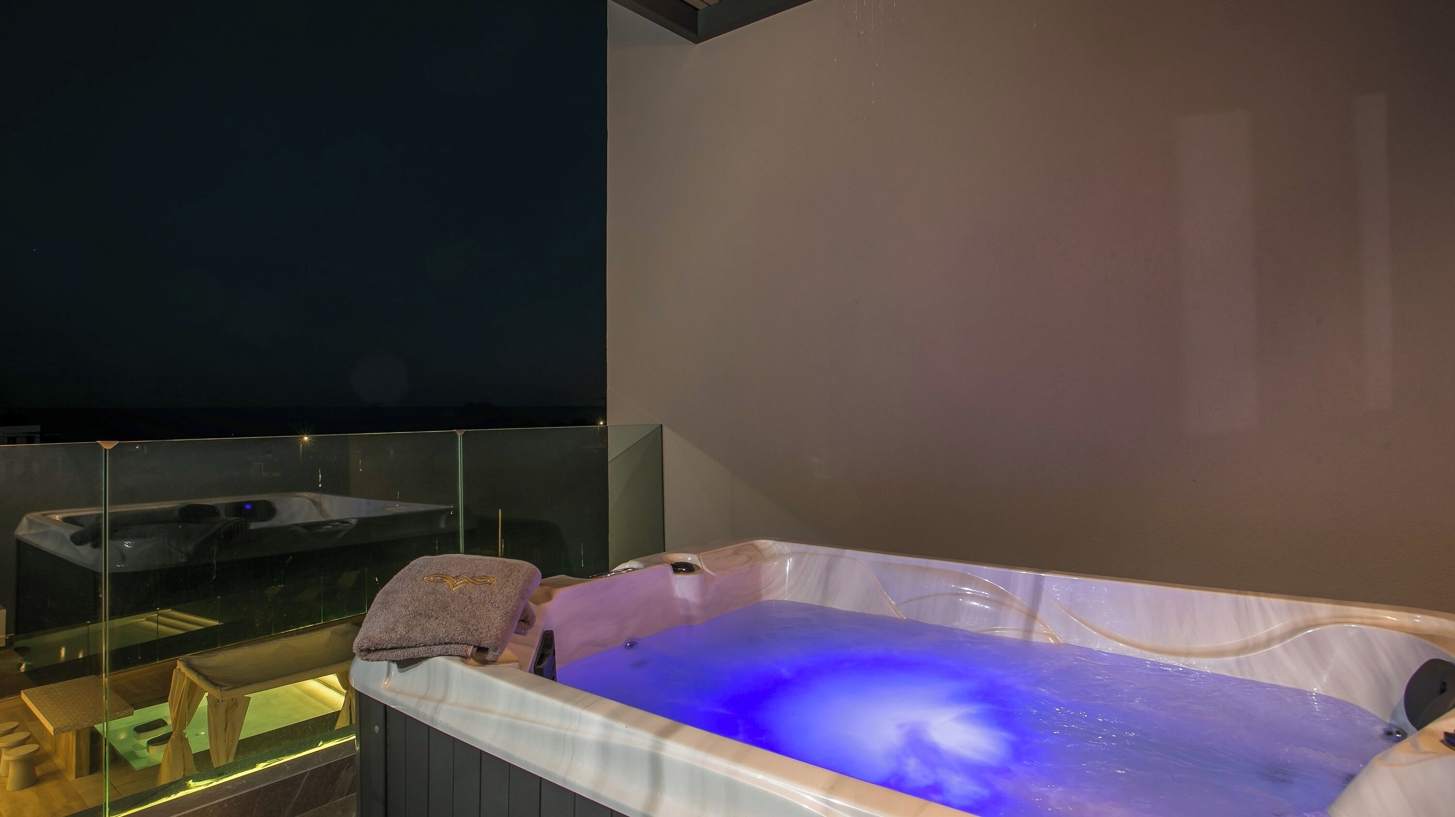Een wellnessruimte met een jacuzzi, een glazen wand en een houten bank.