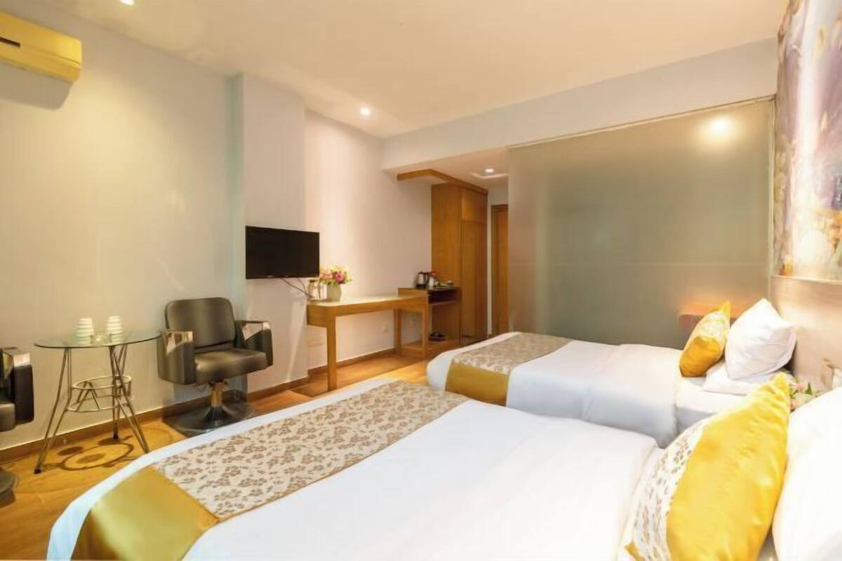 Quarto de hotel com duas camas, uma escrivaninha, uma cadeira, uma TV e uma pequena mesa com chávenas.