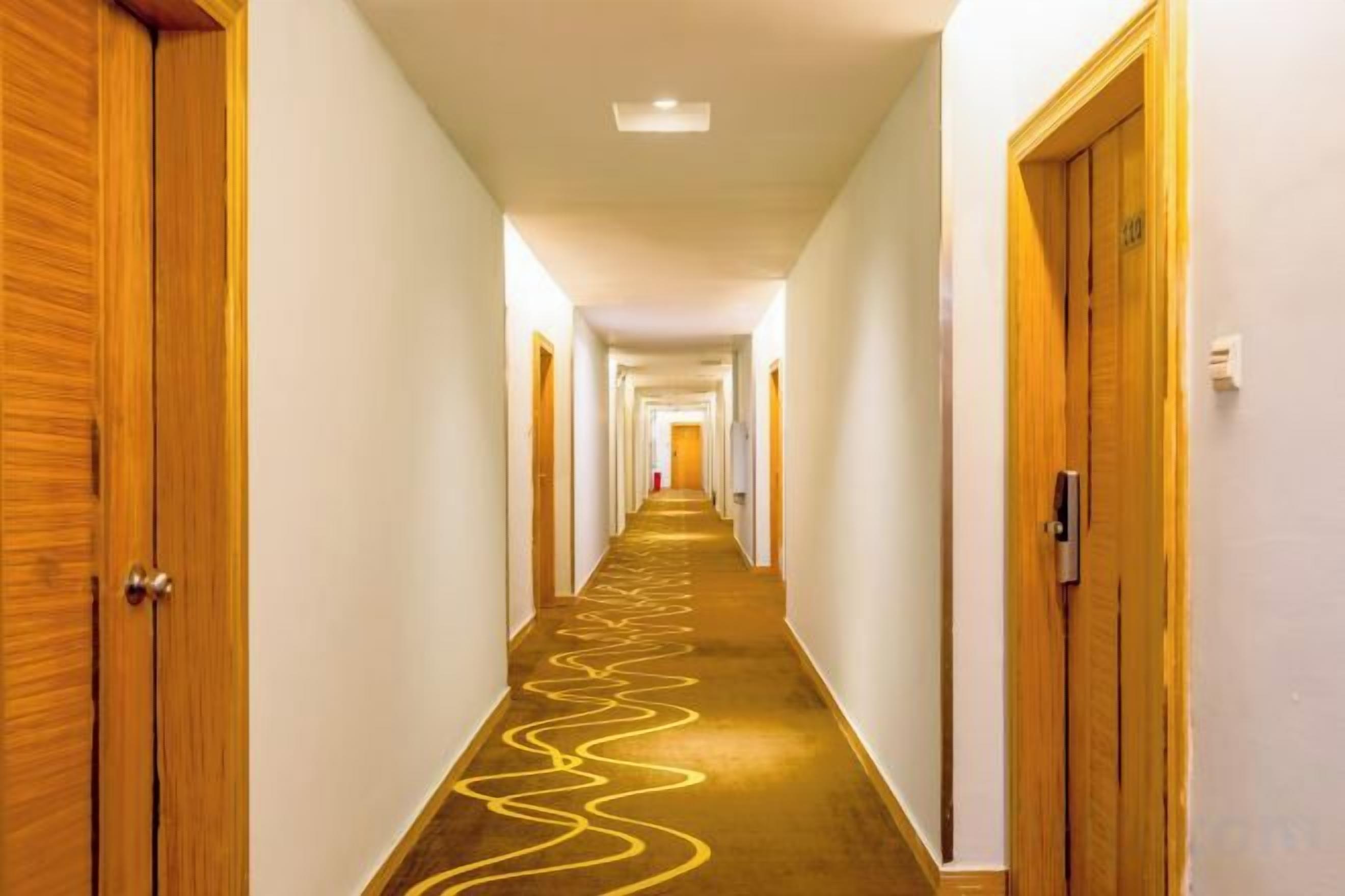 A hotel corridor with wooden doors, a carpeted floor, and a light fixture on the ceiling.