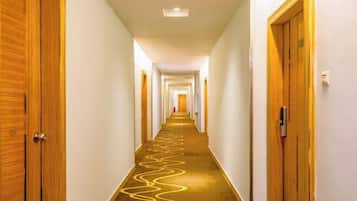 A hotel corridor with wooden doors, a carpeted floor, and a light fixture on the ceiling.