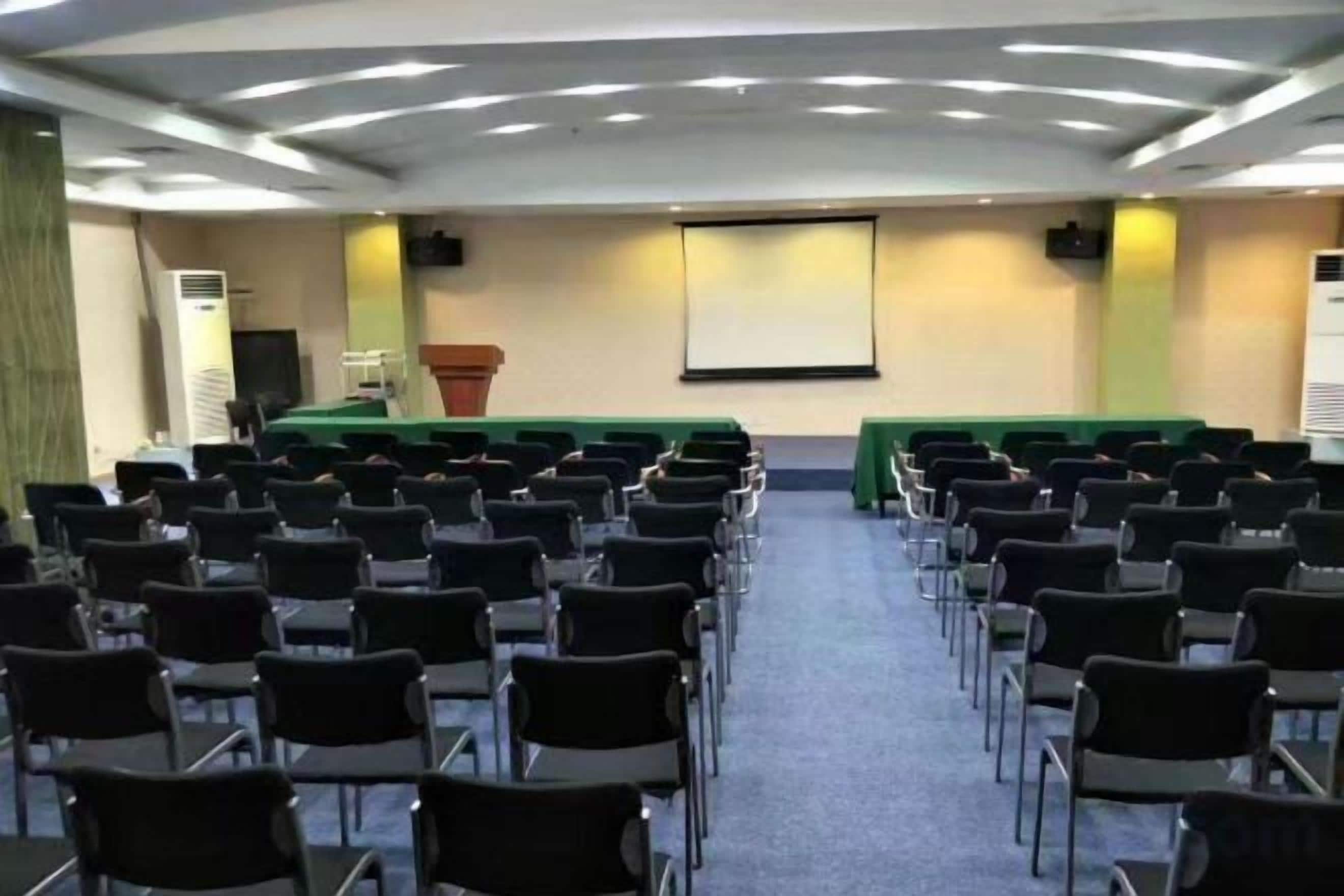 A conference room with rows of chairs, a podium, and a screen at the front.