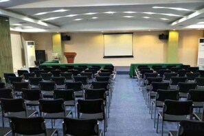 Una sala de conferències amb files de cadires, un escenari i una pantalla al capdavant.