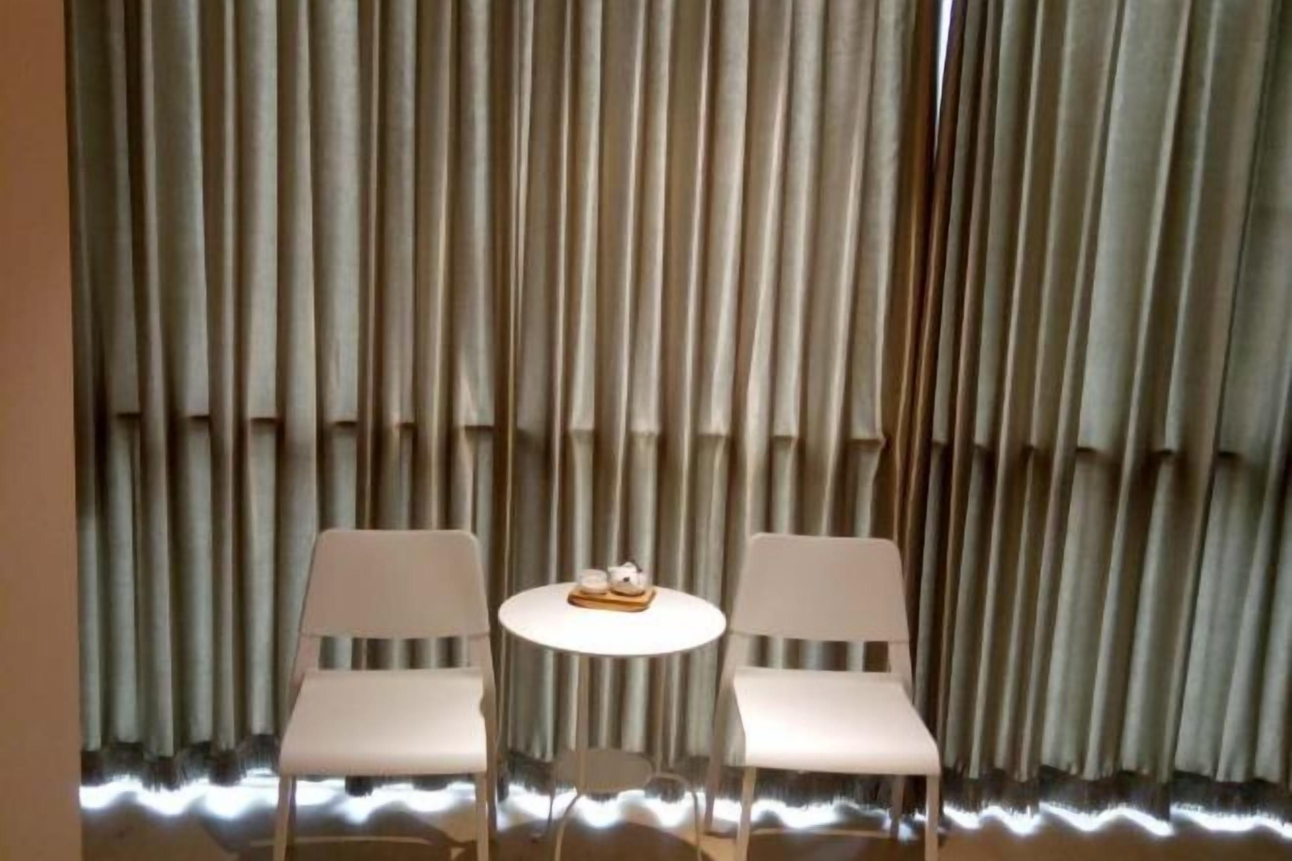 Dos sillas blancas y una pequeña mesa redonda frente a un muro cortina con persianas verticales.