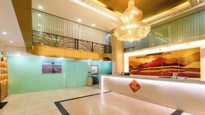 A hotel lobby with a reception desk, a chandelier, a staircase, and a large painting on the wall.