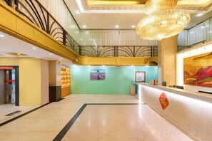 Un vestíbulo de hotel con una recepción, una escalera y una gran lámpara de araña.