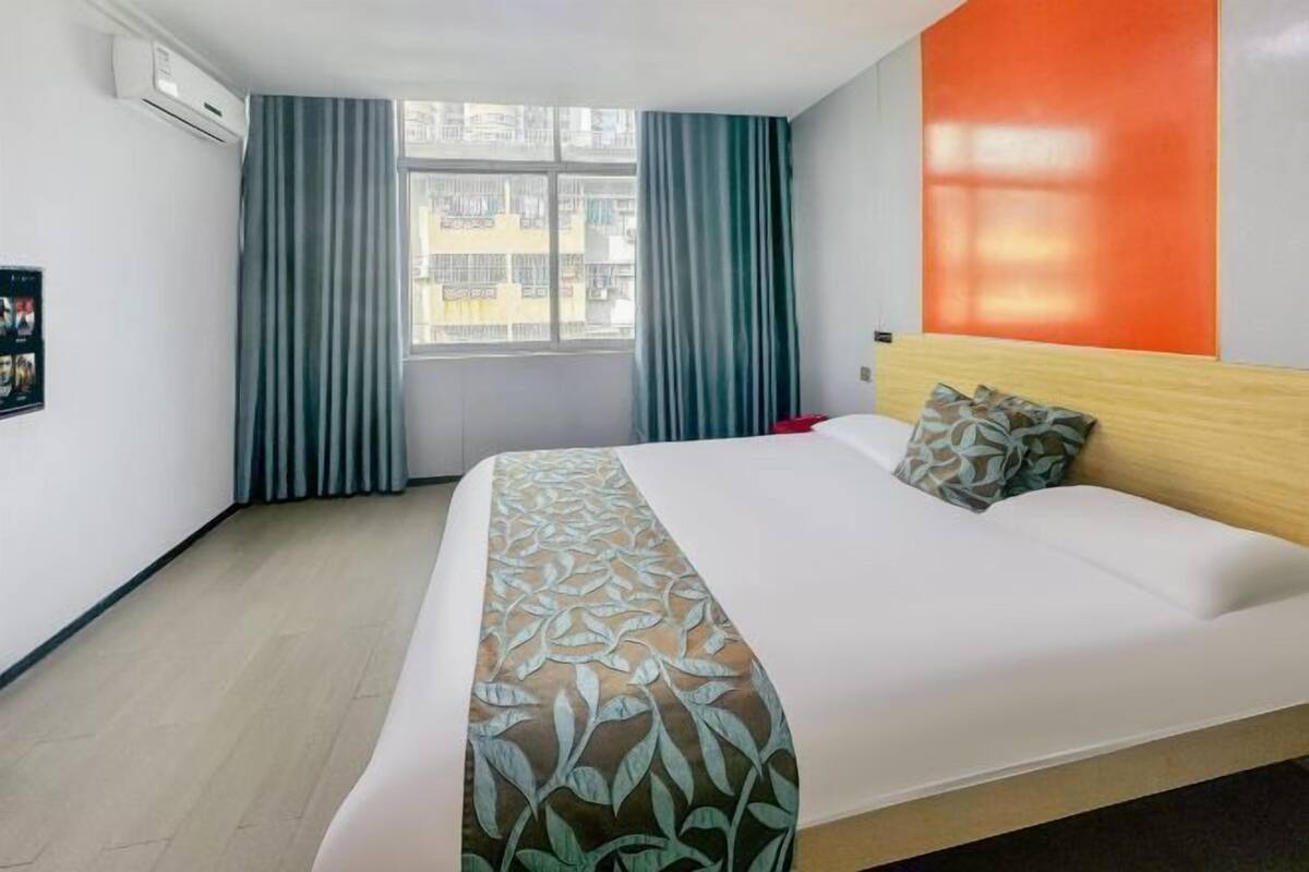 Quarto de hotel com cama, cortinas, janela e ar-condicionado fixado na parede.