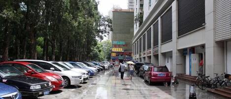 A row of parked cars along a sidewalk with trees on one side and a building with a sign on the other.