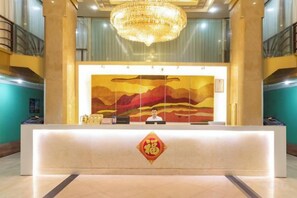 A hotel reception desk with a large artwork above it, a chandelier, and a decorative emblem on the desk. - Silver Spring Hotel (Shenzhen Yuanling Subway Station) (Shenzhen)