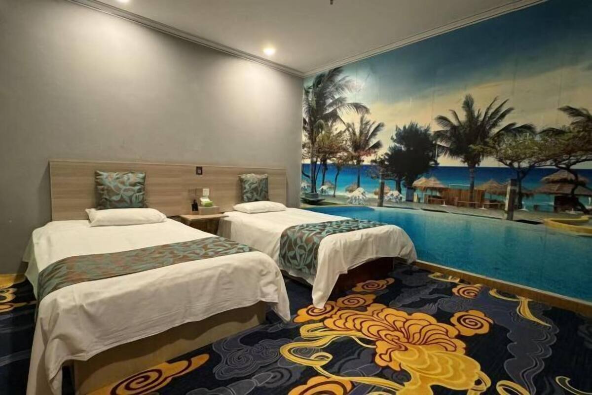 Quarto de hotel com duas camas, um quadro grande de uma cena de praia e vista para a piscina.