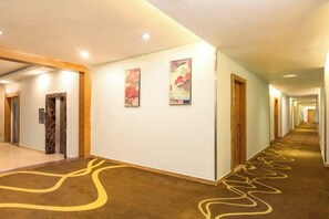 A hotel hallway with a carpeted floor, doors on the right, and artwork on the walls. - Silver Spring Hotel (Shenzhen Yuanling Subway Station) (Shenzhen)
