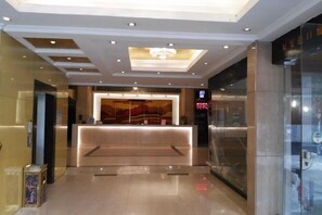 A hotel reception area with a reception desk, a chandelier, and a glass wall on the right.