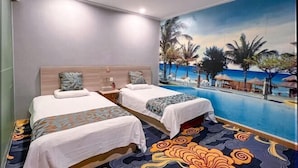 A hotel room with two beds, a large mural of a beach scene, and an infinity pool.