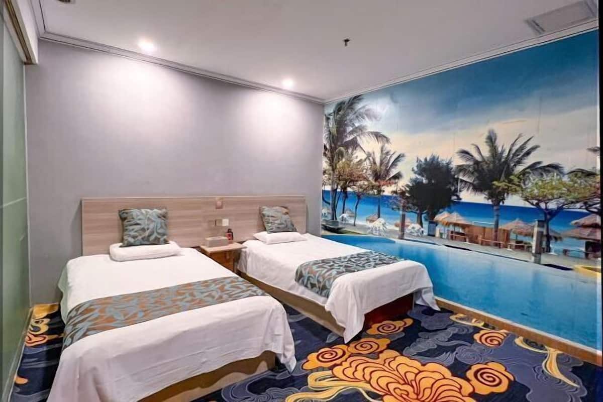 Quarto de hotel com duas camas, um mural grande com paisagem de praia e uma piscina infinita.