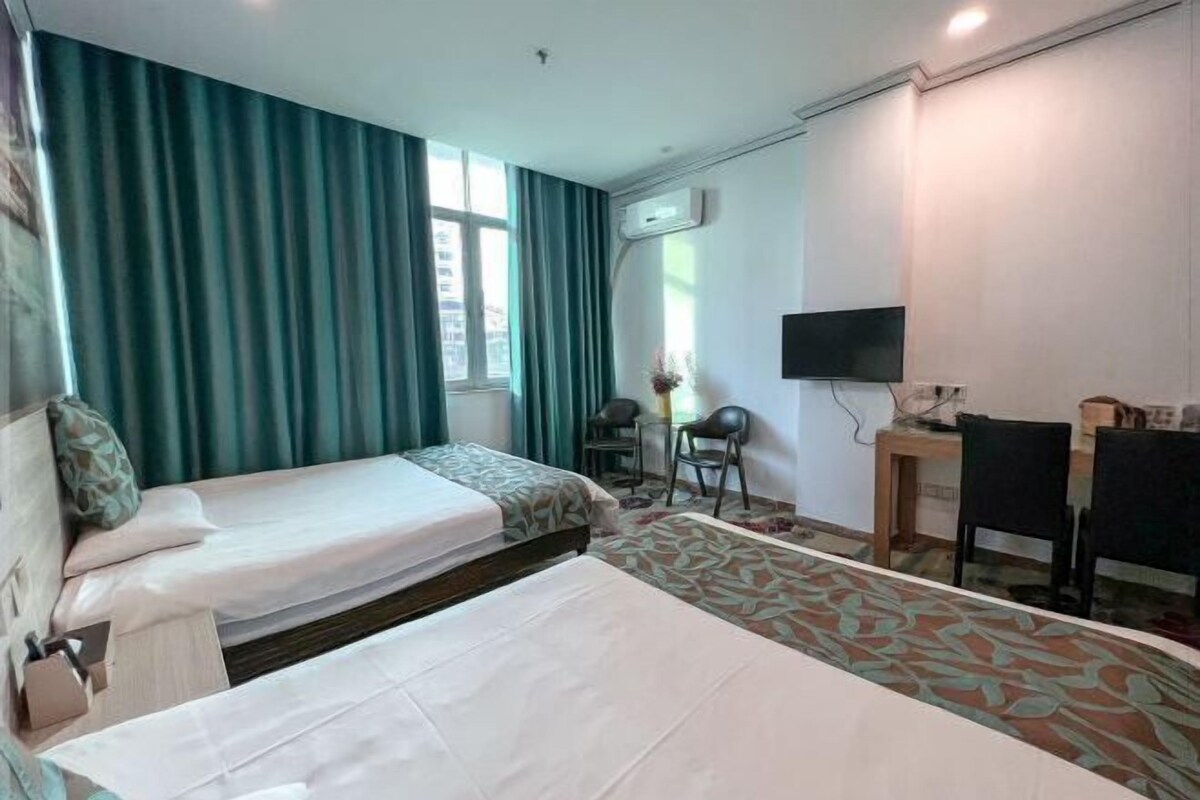 Ein Hotelzimmer mit zwei Betten, einem Schreibtisch, einem Stuhl, einem Fernseher und einem Fenster mit Vorhängen.