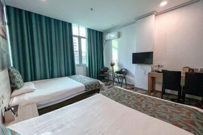 Ein Hotelzimmer mit zwei Betten, einem Schreibtisch, einem Stuhl, einem Fernseher und einem Fenster mit Vorhängen.