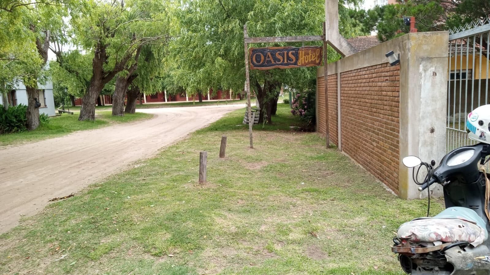 Schild für das Hotel OASIS, eine gepflasterte Straße und ein abgestellter Roller.