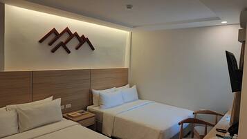 A hotel room with two beds, a wooden headboard, a wall-mounted TV, and a table with a chair.