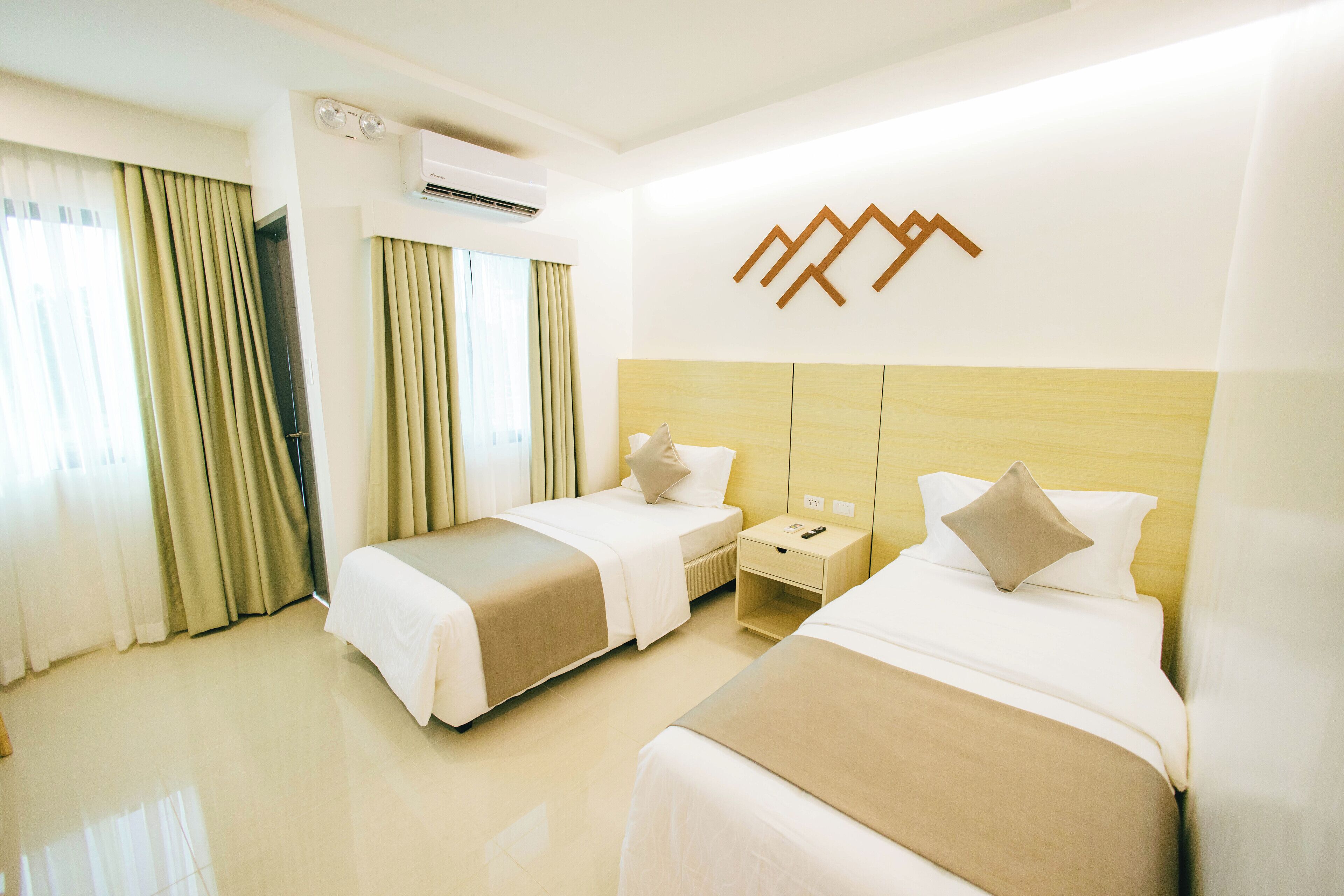 A hotel room with two beds, a wooden headboard, a nightstand, and a wall-mounted air conditioner.