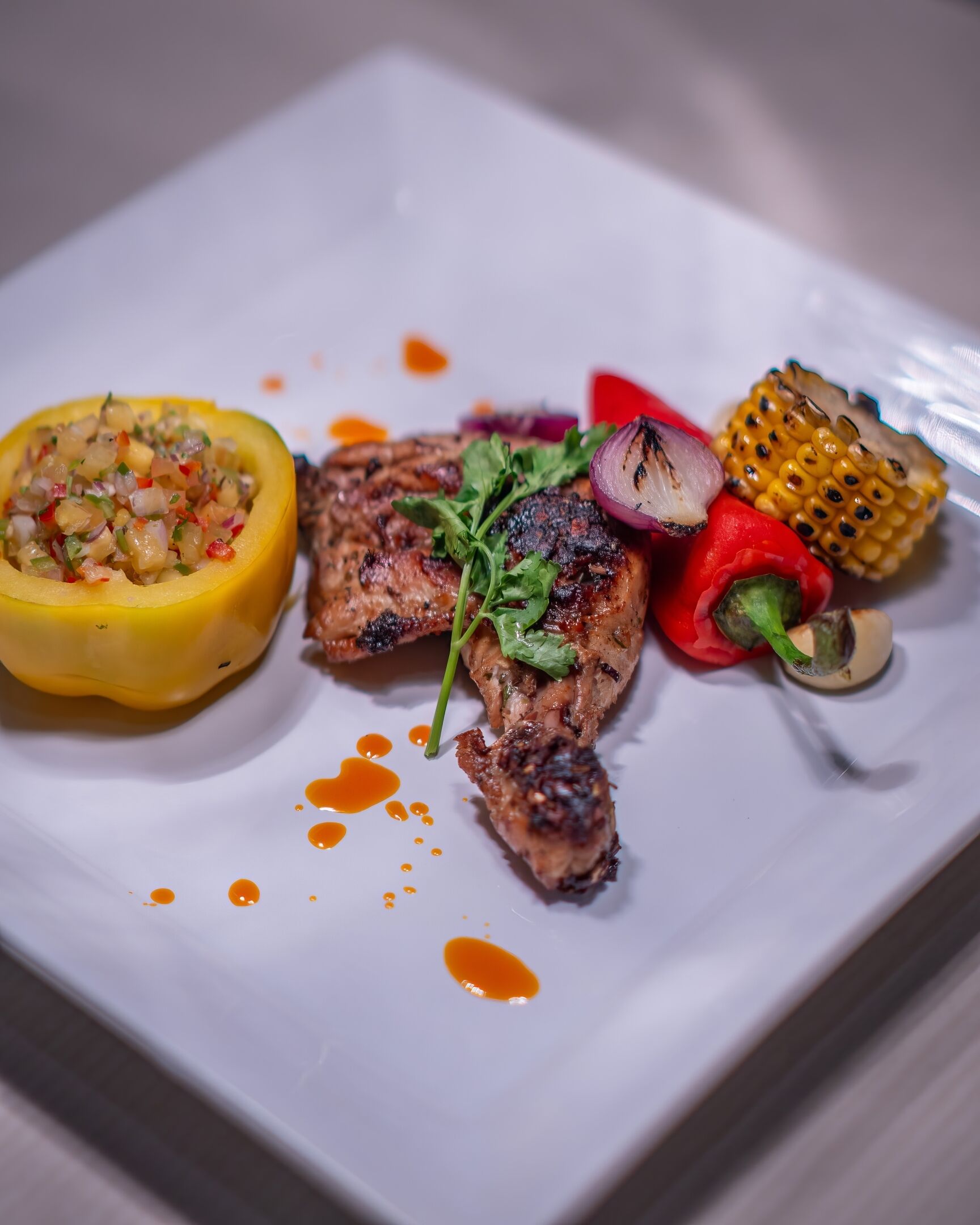 A plate with grilled chicken, a stuffed bell pepper, grilled vegetables, and a corn on the cob.