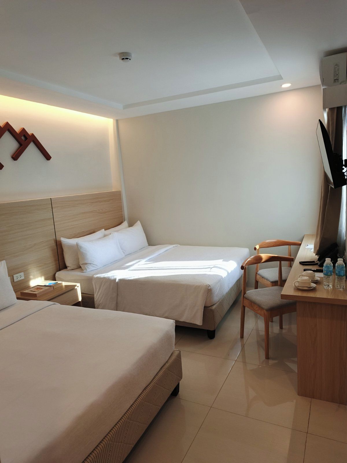 A hotel room with two beds, a desk, a chair, and a television.
