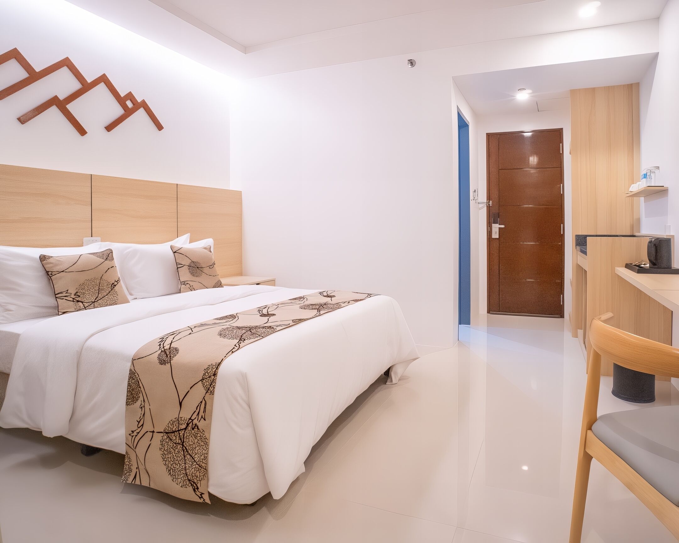 A modern hotel room with a large bed, a wooden headboard, a bedside table, and a small desk with a chair.