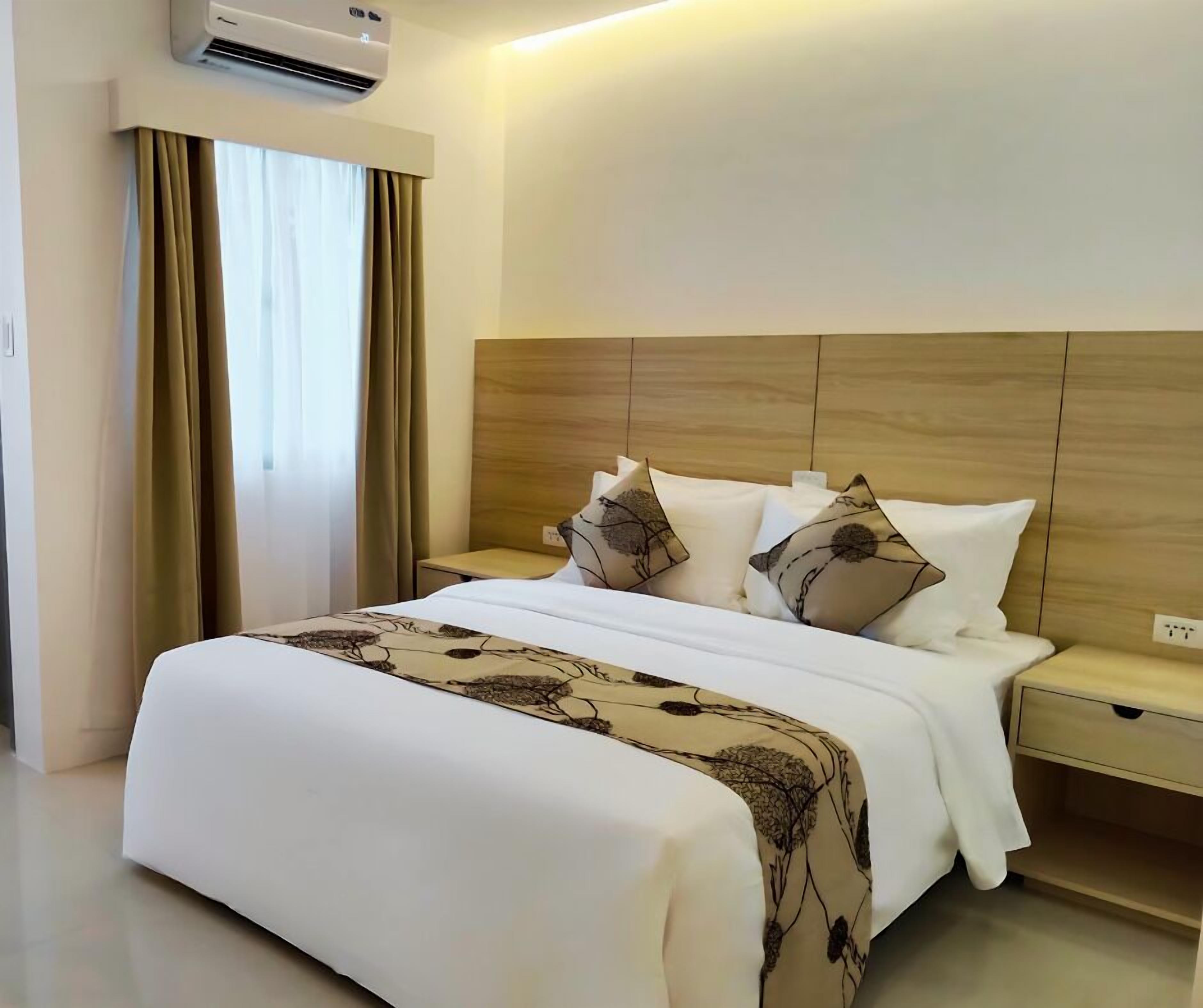 A hotel room with a bed, bedside tables, and an air conditioning unit.