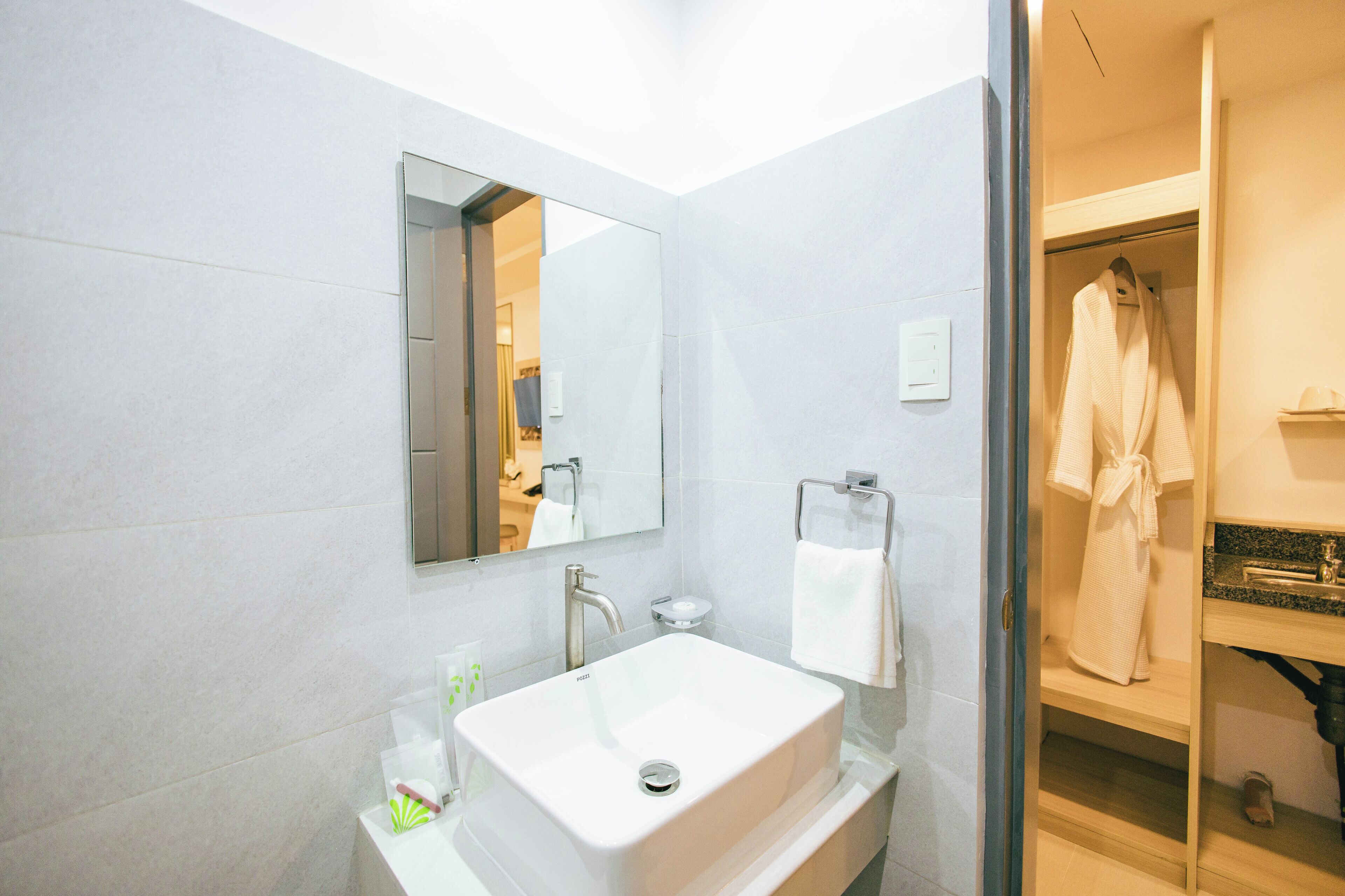 A modern bathroom with a large mirror, a white sink, and a robe hanging on a rack.