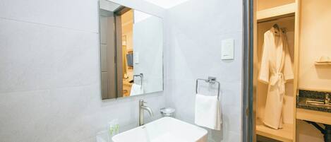 A modern bathroom with a large mirror, a white sink, and a robe hanging on a rack.