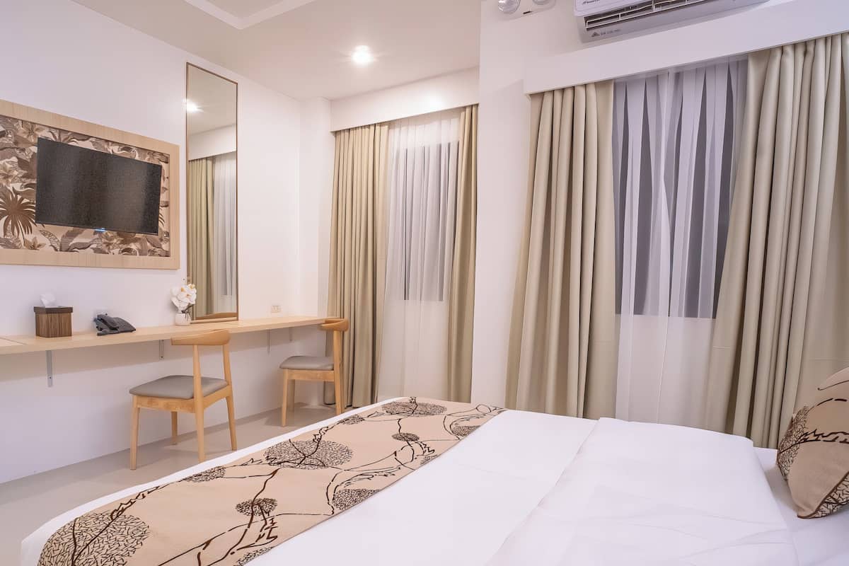 Una habitación de hotel con cama, escritorio, silla, espejo y cortinas.
