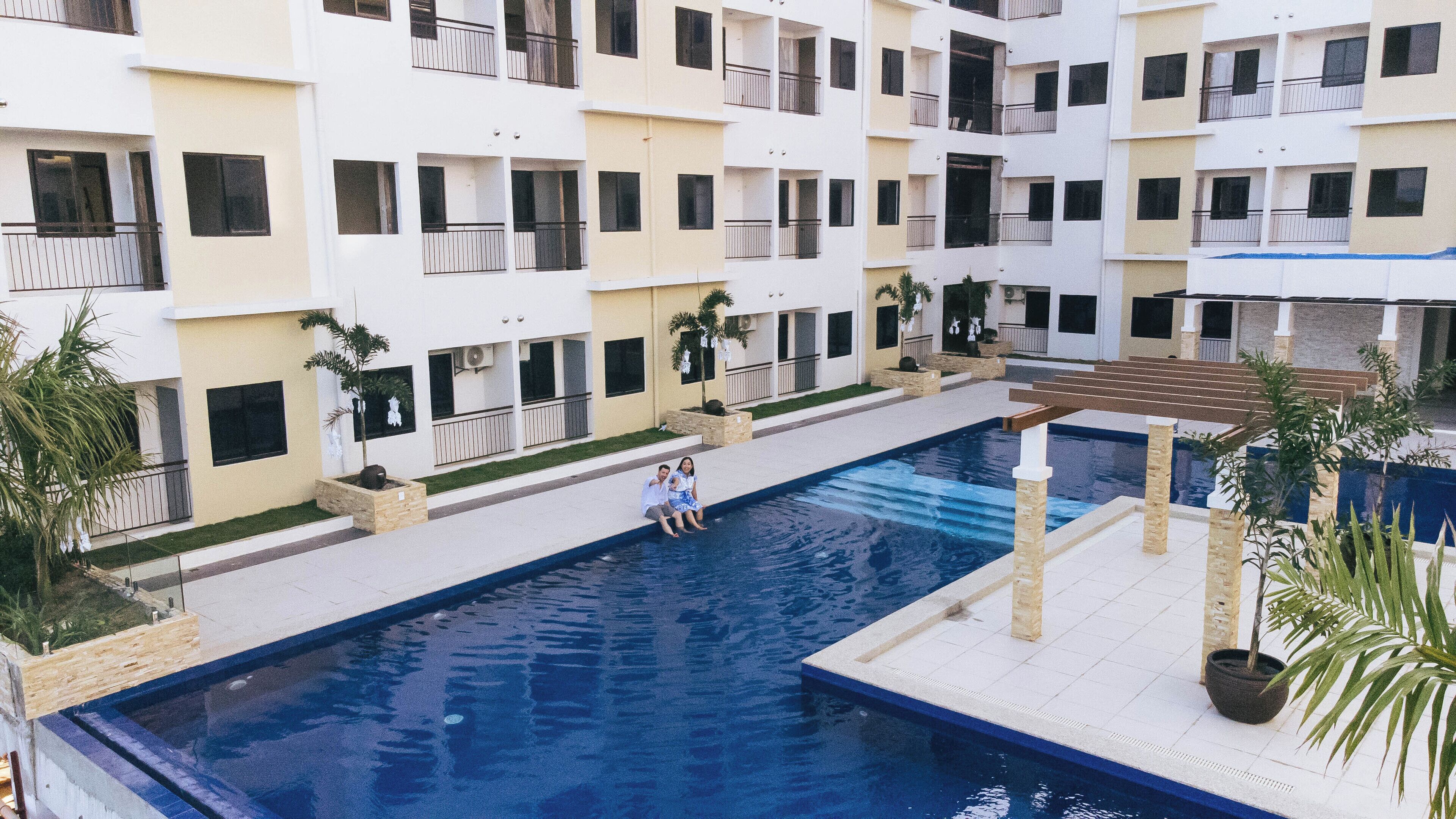Uma piscina cercada por um edifício com várias andares, varandas e plantas em vasos.