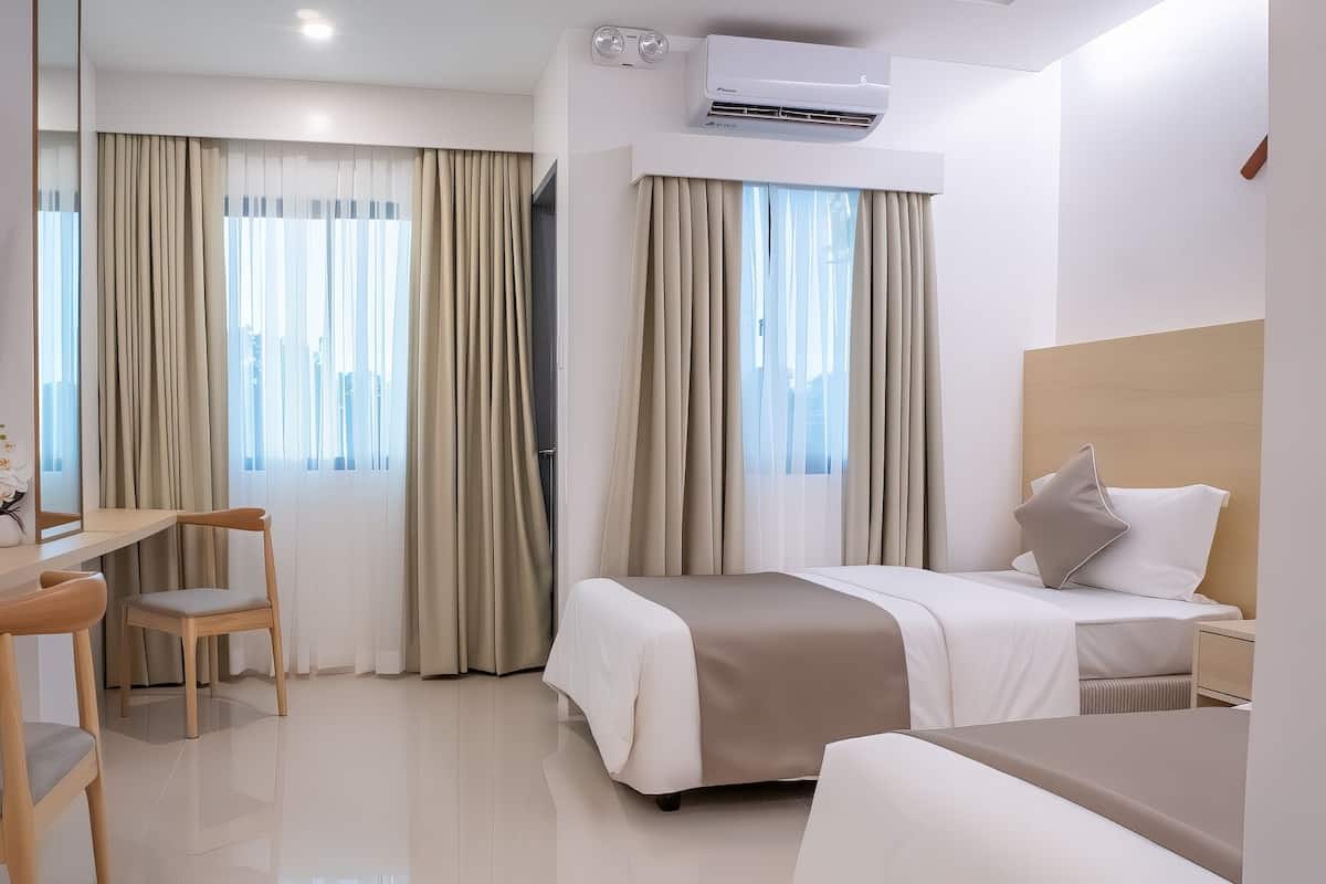 Una habitación de hotel moderna con una cama, un escritorio y una silla. Hay un aire acondicionado en la pared y una ventana con cortinas.