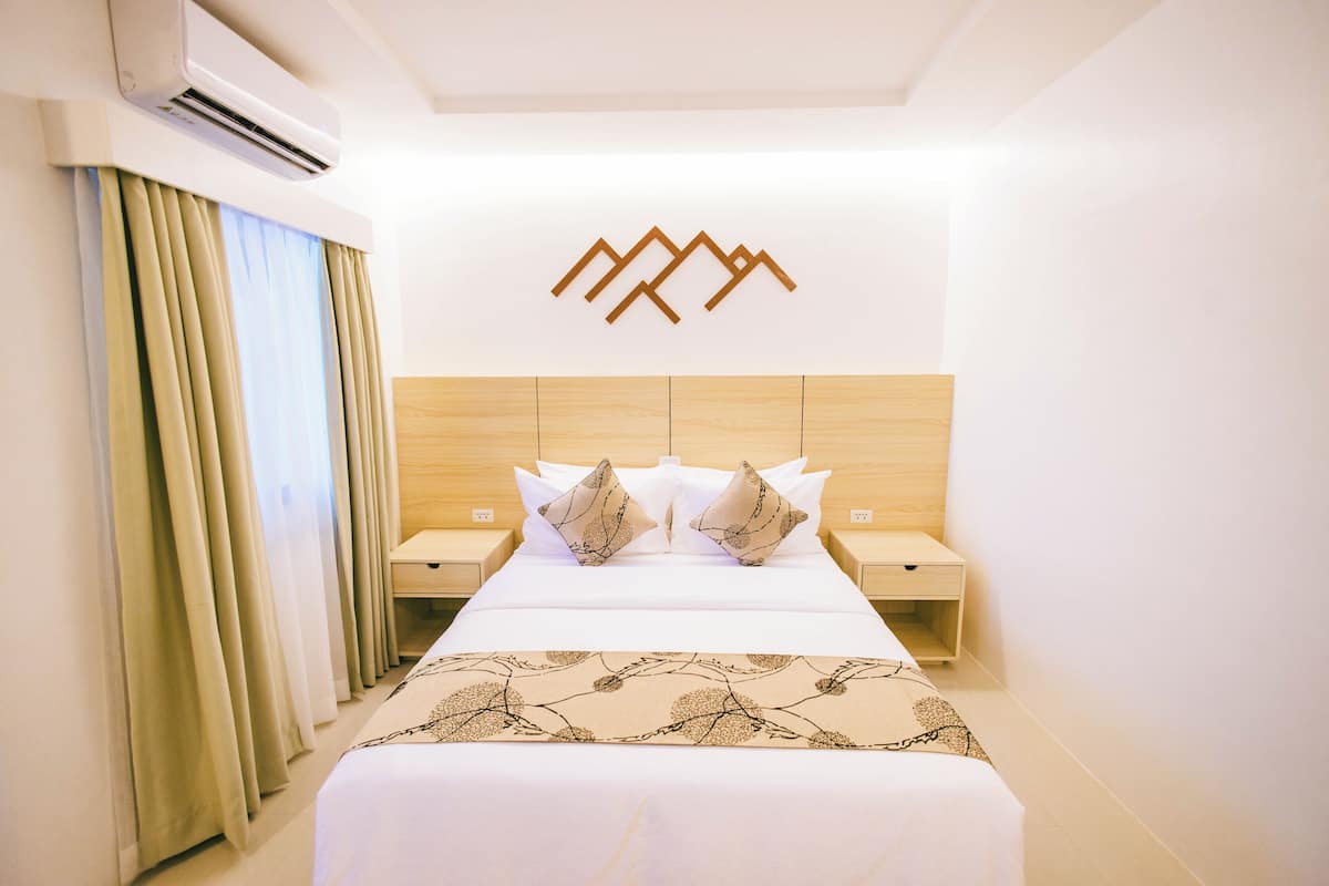 Habitación de hotel con cama, dos mesitas de noche, aire acondicionado instalado en la pared y un adorno mural.