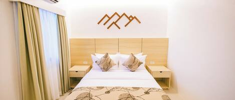 Habitación de hotel con cama, dos mesitas de noche, aire acondicionado instalado en la pared y un adorno mural.