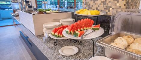 Montaje de buffet con rodajas de sandía, fruta amarilla y platos de carne.