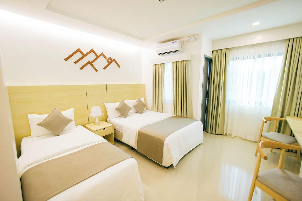 Habitación de hotel con dos camas, un escritorio y un equipo de aire acondicionado.