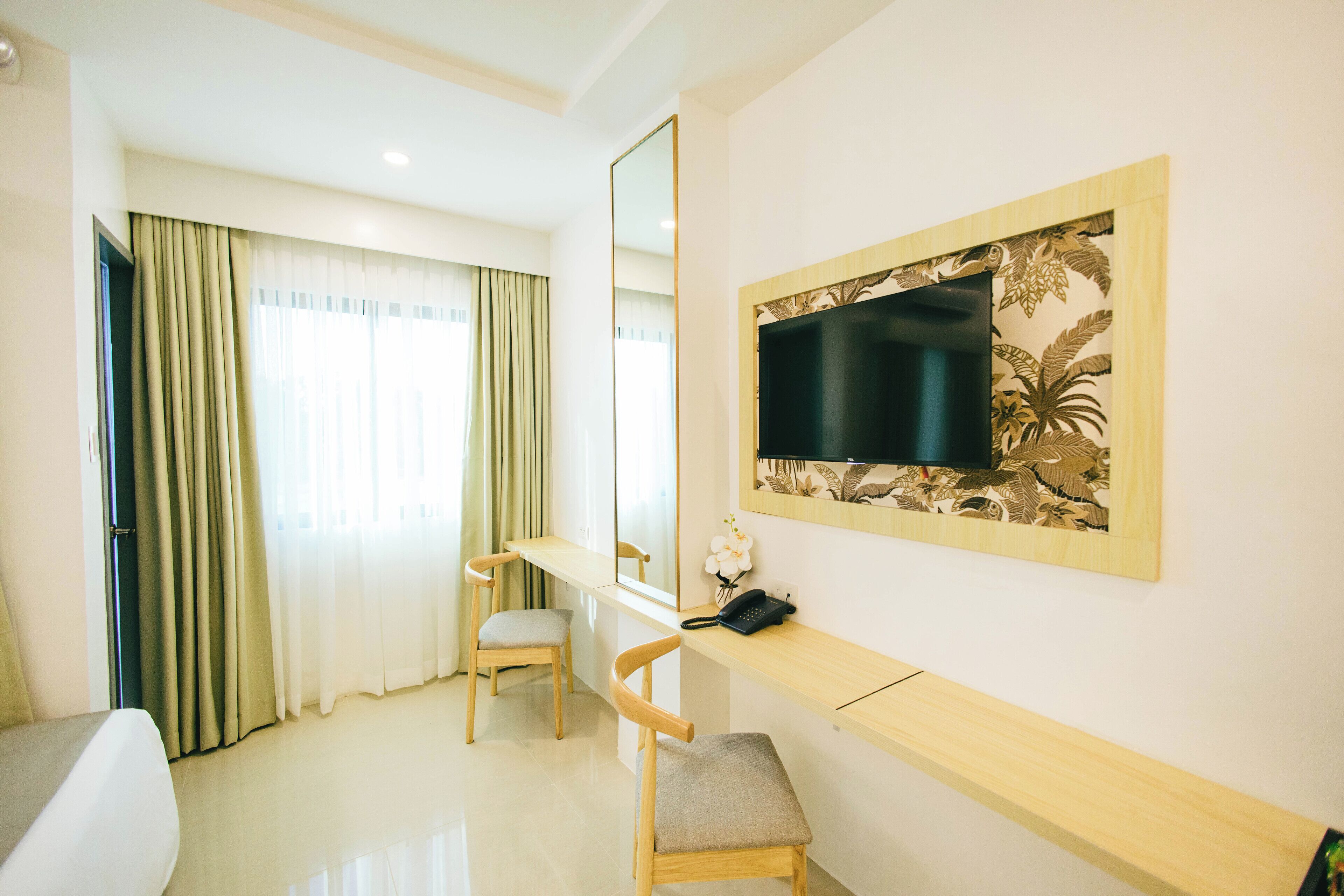 A hotel room with a bed, a desk, a chair, a TV, and a window with curtains.